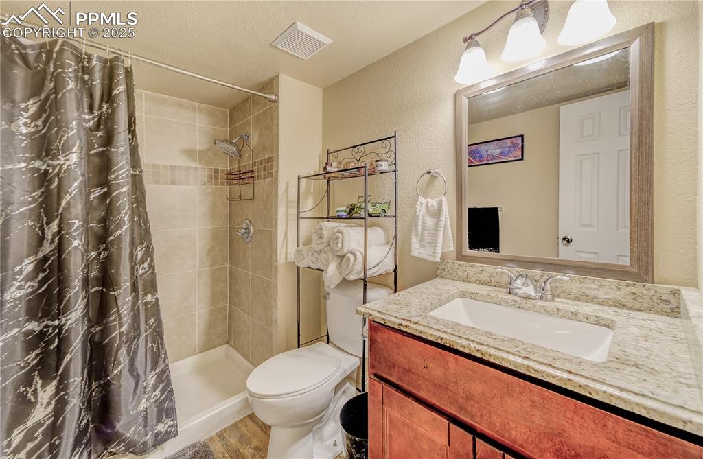 Bathroom featuring vanity, a textured ceiling, hardwood / wood-style flooring, walk in shower, and toilet