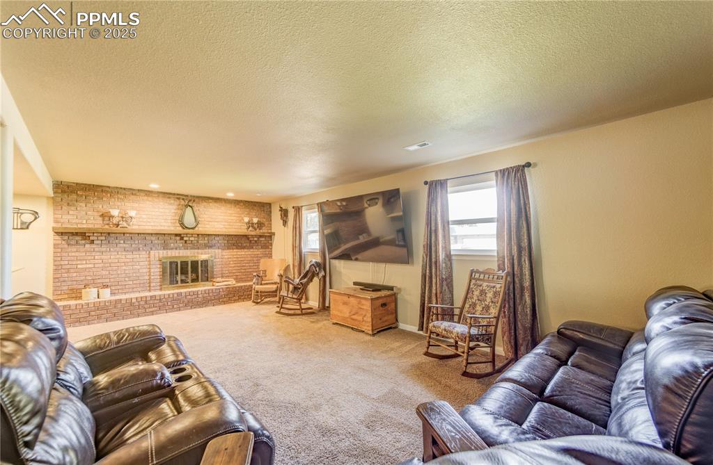 Carpeted living room featuring a brick fireplace, a textured ceiling, and brick wall