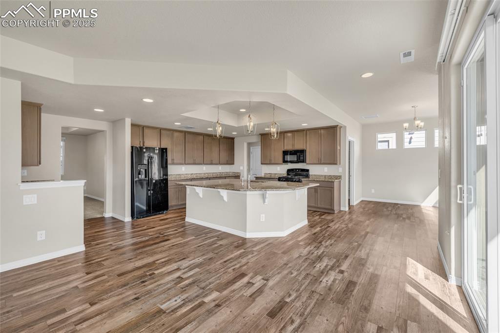 Kitchen featuring a chandelier, hanging light fixtures, black appliances, a kitchen island with sink, and recessed lighting
