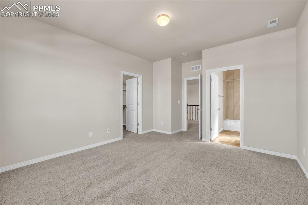 Unfurnished bedroom with a walk in closet, light colored carpet, and connected bathroom