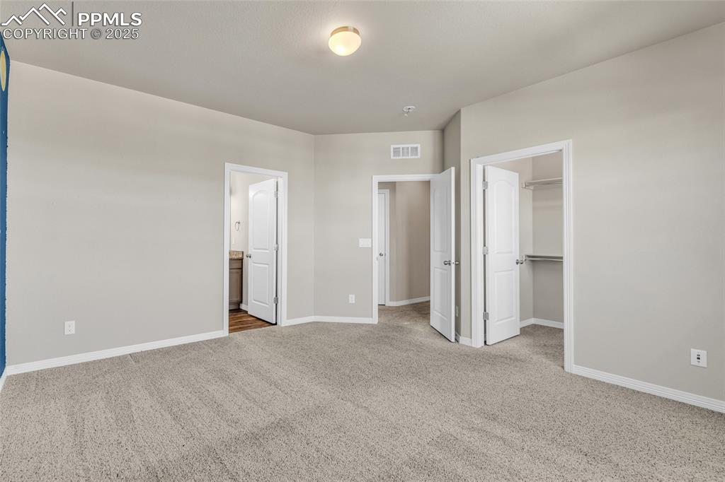 Unfurnished bedroom featuring a spacious closet, light carpet, and ensuite bath