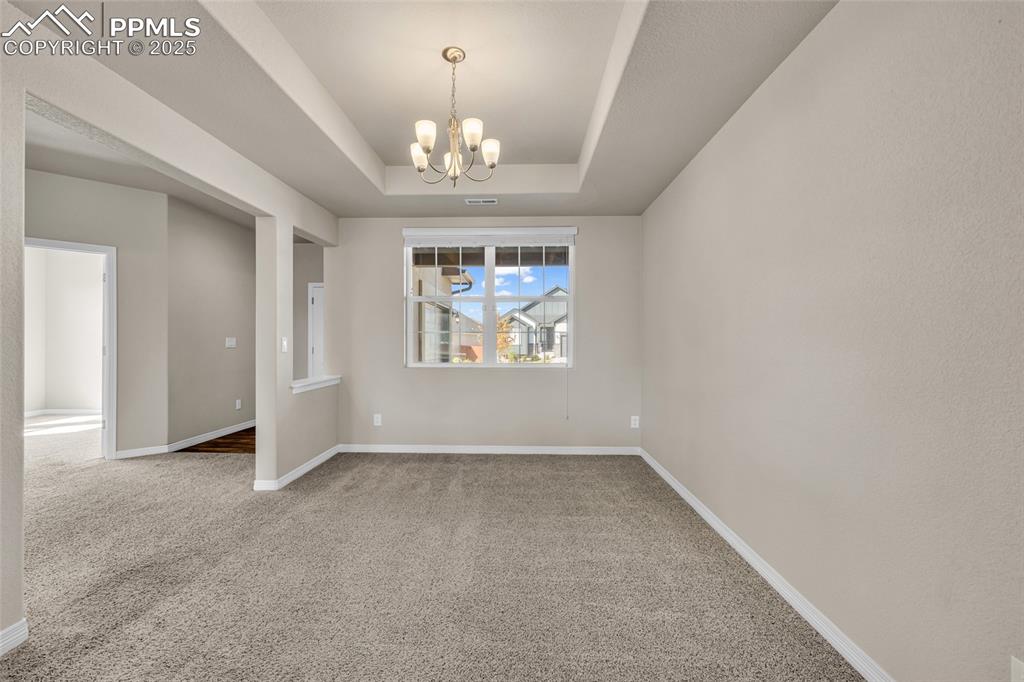 Empty room with carpet, a raised ceiling, and a chandelier