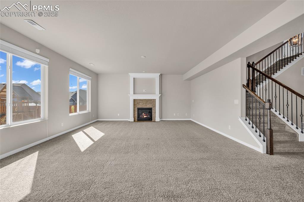 Unfurnished living room with stairs, a fireplace, and carpet flooring