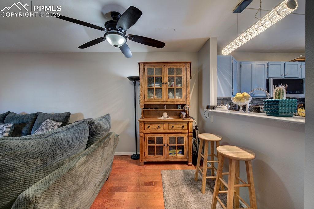 Dining area with lighted ceiling fan, wood laminate floor, and breakfast bar.