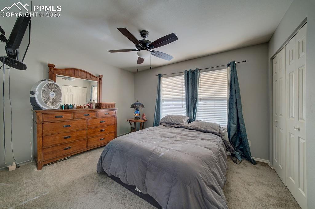 Primary Suite with neutral carpet, a lighted ceiling fan, double closets, and adjoining bathroom.