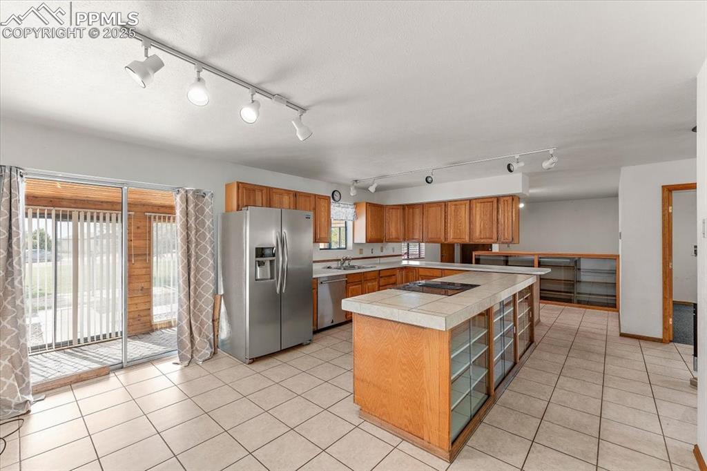 Kitchen with appliances with stainless steel finishes, rail lighting, brown cabinets, a kitchen island, and light tile patterned flooring