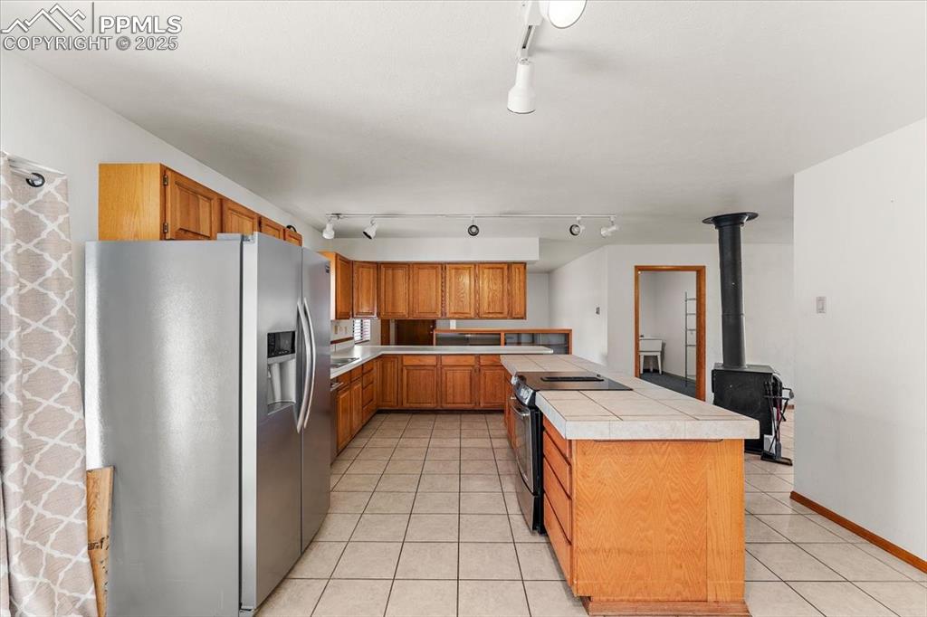 Kitchen featuring stainless steel fridge with ice dispenser, brown cabinets, black range with electric cooktop, track lighting, and light tile patterned flooring