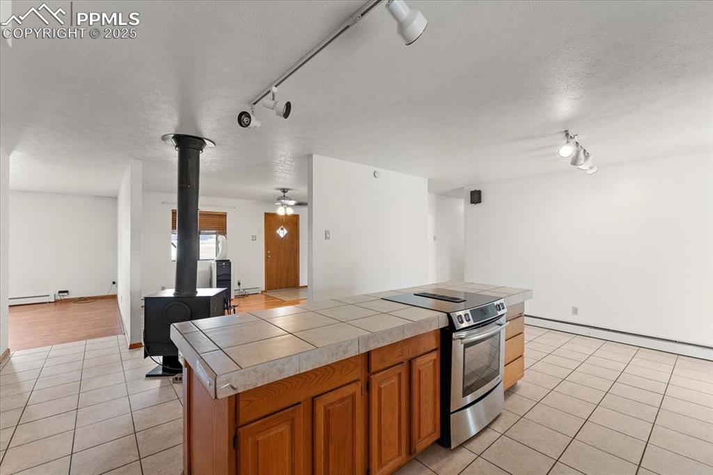 Kitchen with track lighting, stainless steel electric range, light tile patterned floors, brown cabinetry, and a textured ceiling