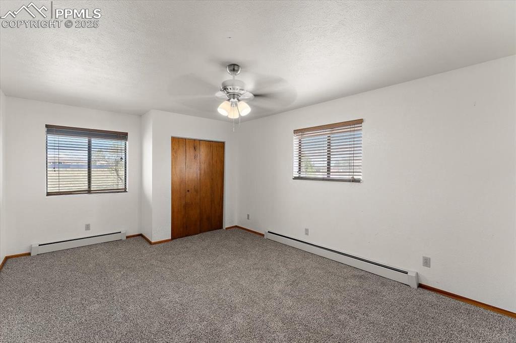 Unfurnished bedroom featuring a baseboard radiator, carpet floors, a textured ceiling, a closet, and ceiling fan