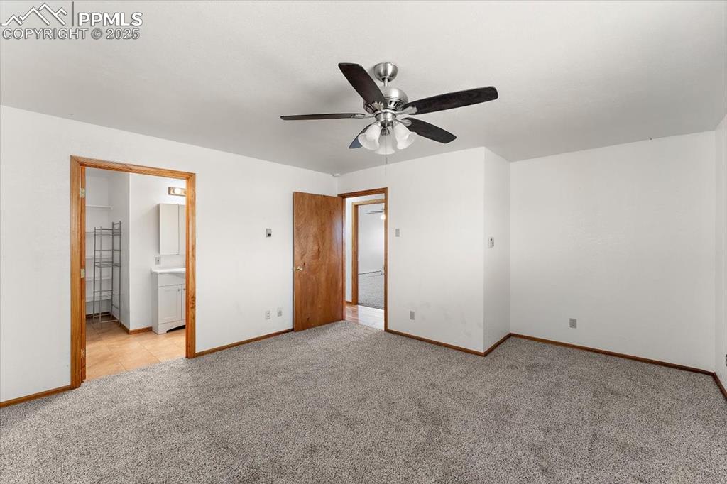 Unfurnished bedroom featuring carpet flooring, ensuite bathroom, and a ceiling fan