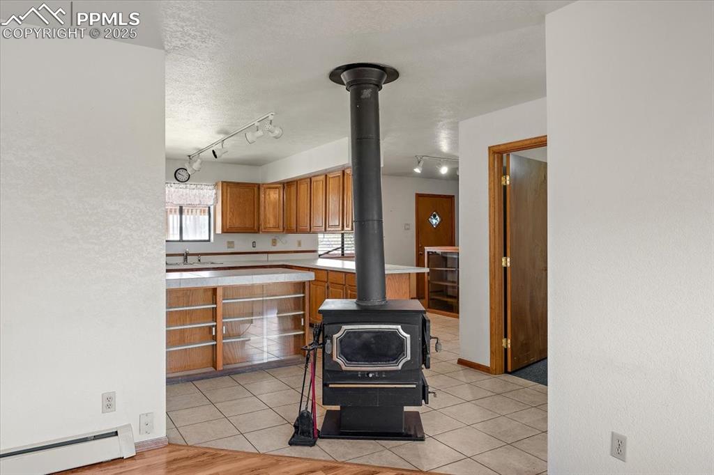 Kitchen featuring brown cabinetry, light tile patterned floors, a baseboard heating unit, a wood stove, and track lighting