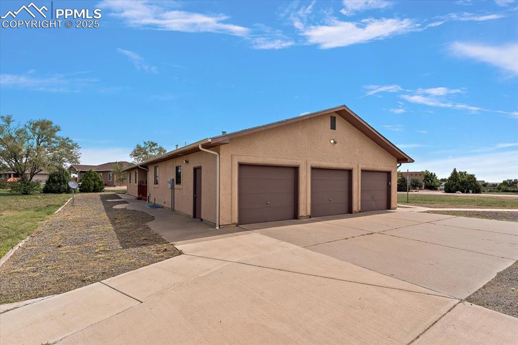 View of side of property with a garage, stucco siding, and concrete driveway