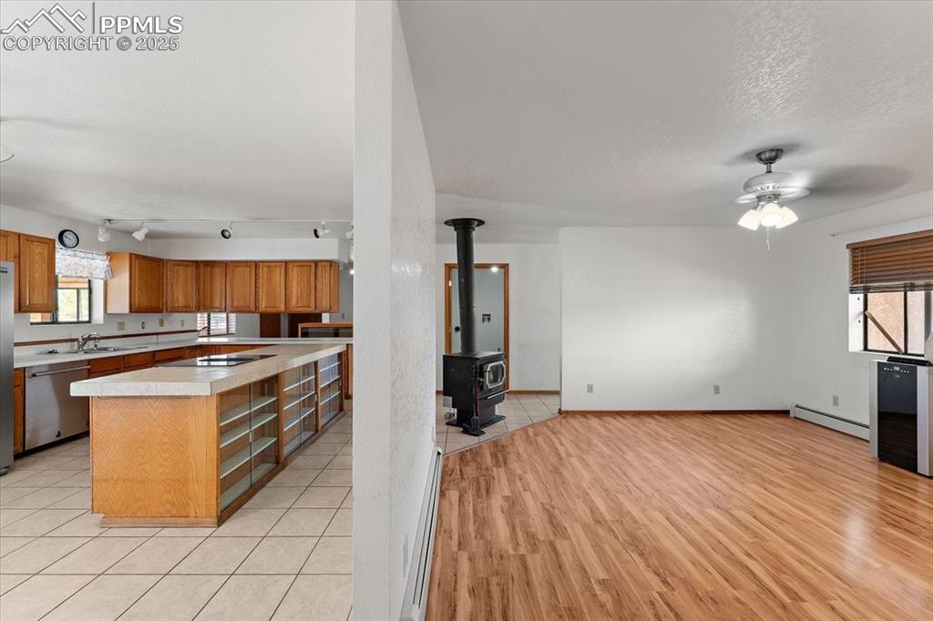 Kitchen with light countertops, brown cabinets, dishwasher, a center island, and a baseboard heating unit