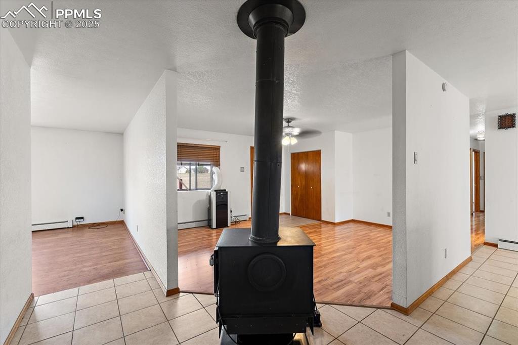 Unfurnished living room featuring light tile patterned floors, a textured ceiling, a wood stove, and a baseboard radiator