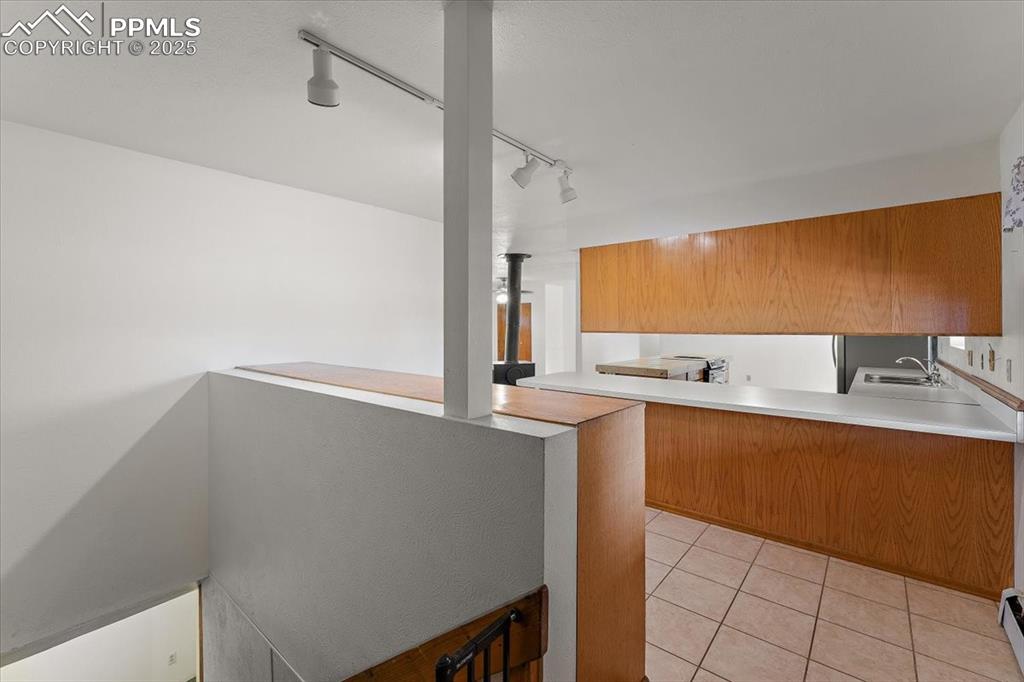 Kitchen with track lighting, light tile patterned flooring, a peninsula, light countertops, and brown cabinetry