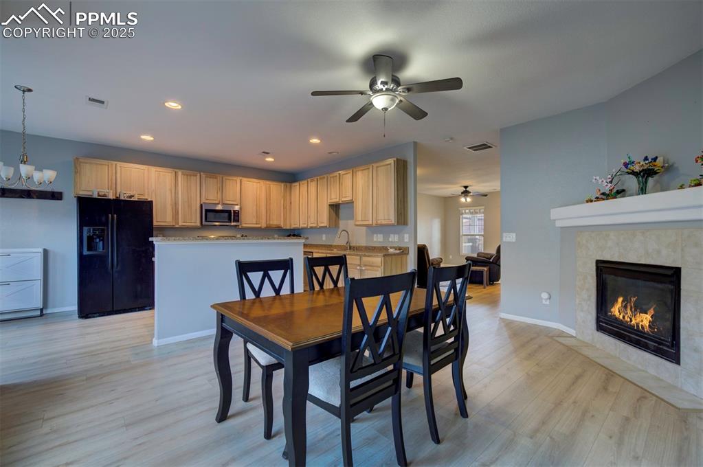 Dining room featuring light wood-style flooring, recessed lighting, a tile fireplace, ceiling fan, and a chandelier