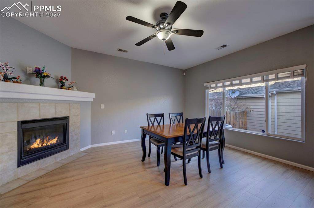 Dining space featuring light wood-type flooring, ceiling fan, and a tiled fireplace