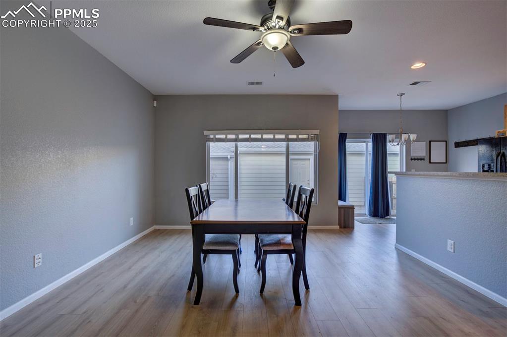Dining area with light wood finished floors, a textured wall, a chandelier, a ceiling fan, and recessed lighting