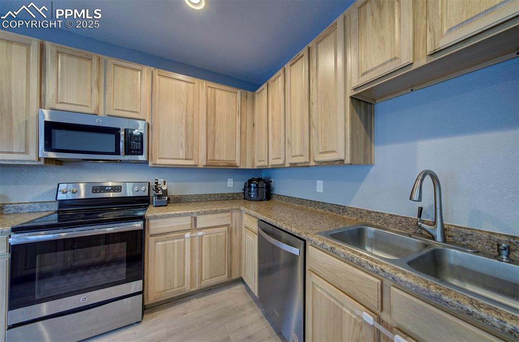 Kitchen with stainless steel appliances, light brown cabinetry, and light wood finished floors