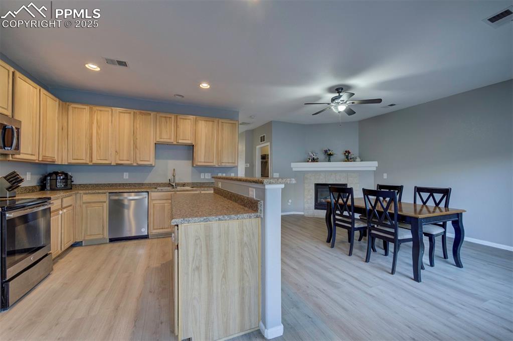 Kitchen featuring appliances with stainless steel finishes, light brown cabinetry, light wood finished floors, a tile fireplace, and recessed lighting
