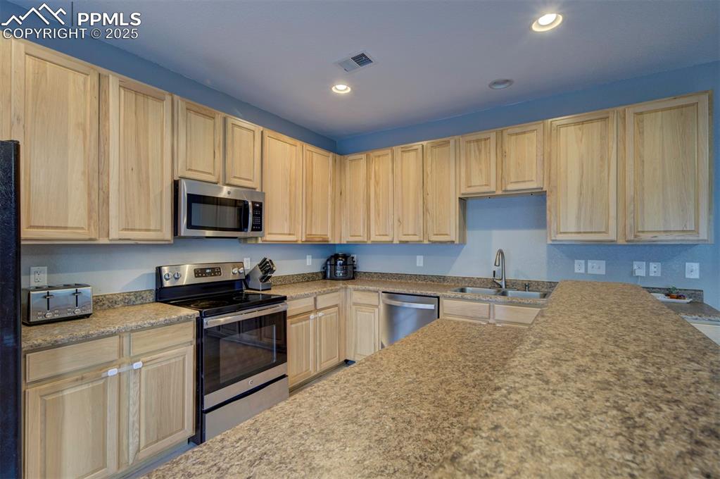 Kitchen with stainless steel appliances, recessed lighting, light brown cabinetry, and light stone countertops