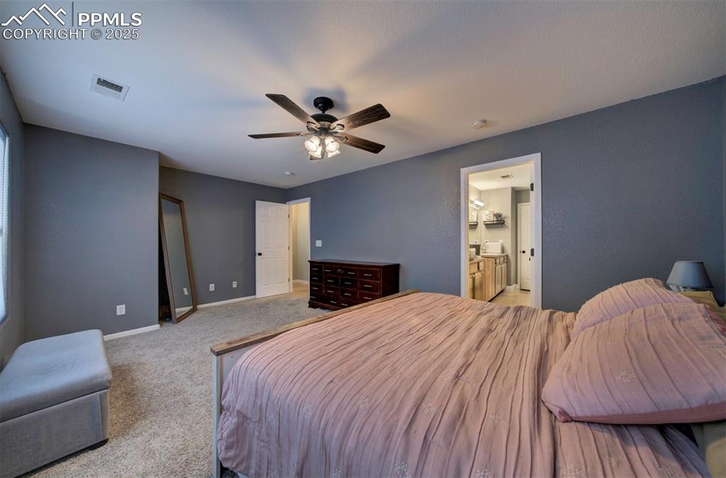 Bedroom featuring ceiling fan, light colored carpet, and ensuite bath