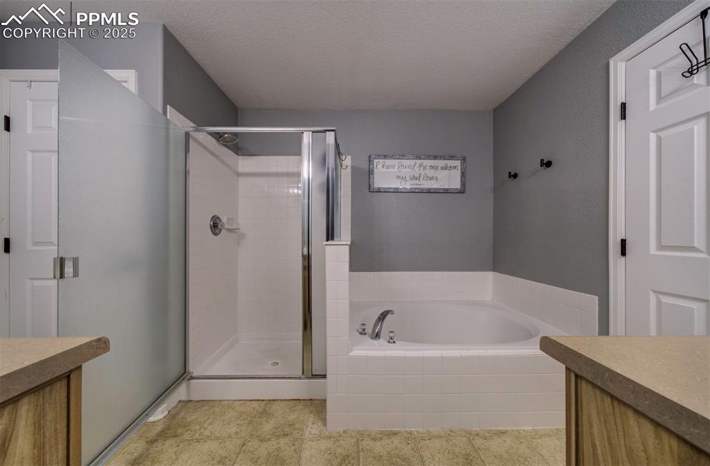 Full bathroom with vanity, a textured ceiling, a bath, a stall shower, and light tile patterned floors