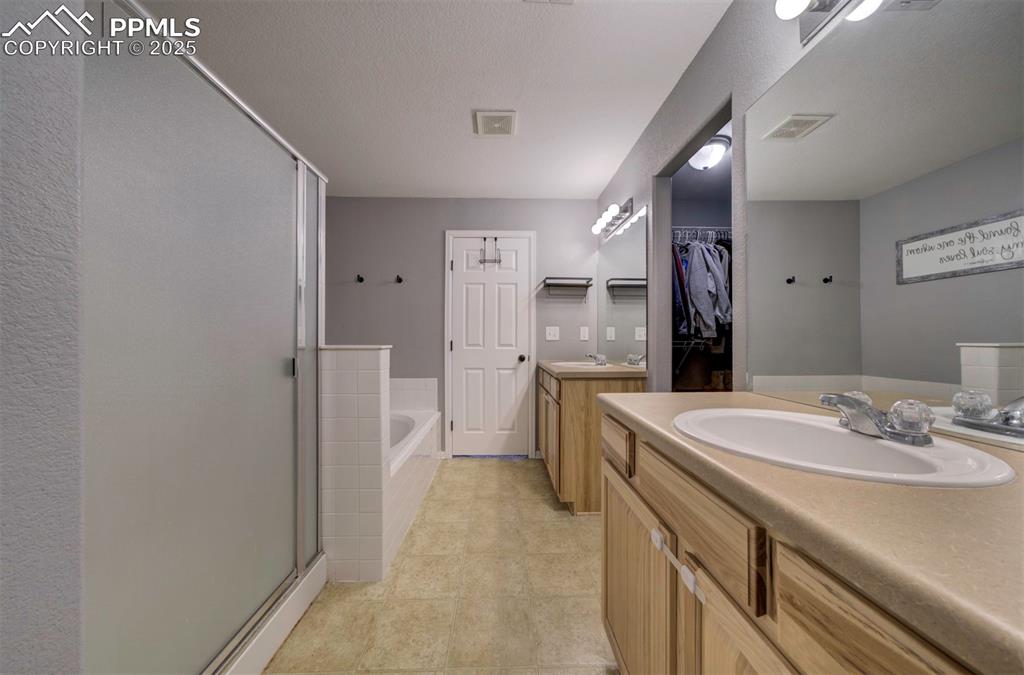 Full bathroom with two vanities, a bath, a shower stall, a spacious closet, and a textured ceiling