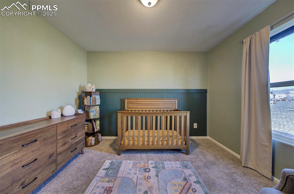 Carpeted bedroom with a nursery area, a textured ceiling, and wainscoting