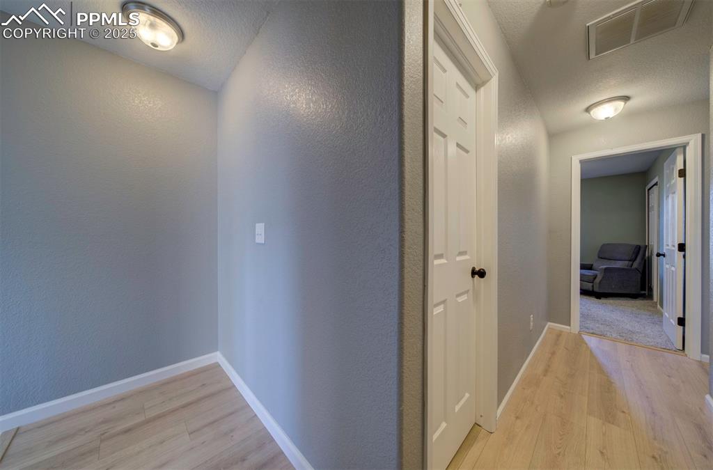 Corridor with light wood-style flooring, a textured wall, and a textured ceiling