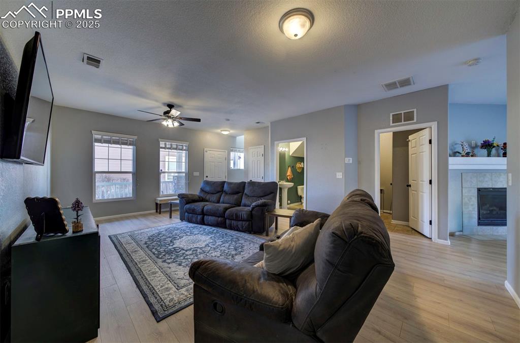 Living area with a tile fireplace, a textured ceiling, light wood finished floors, and a ceiling fan