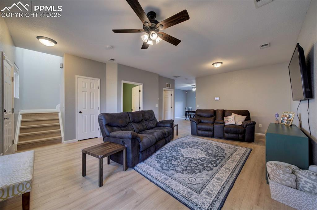 Living room featuring a ceiling fan, stairway, and light wood-type flooring