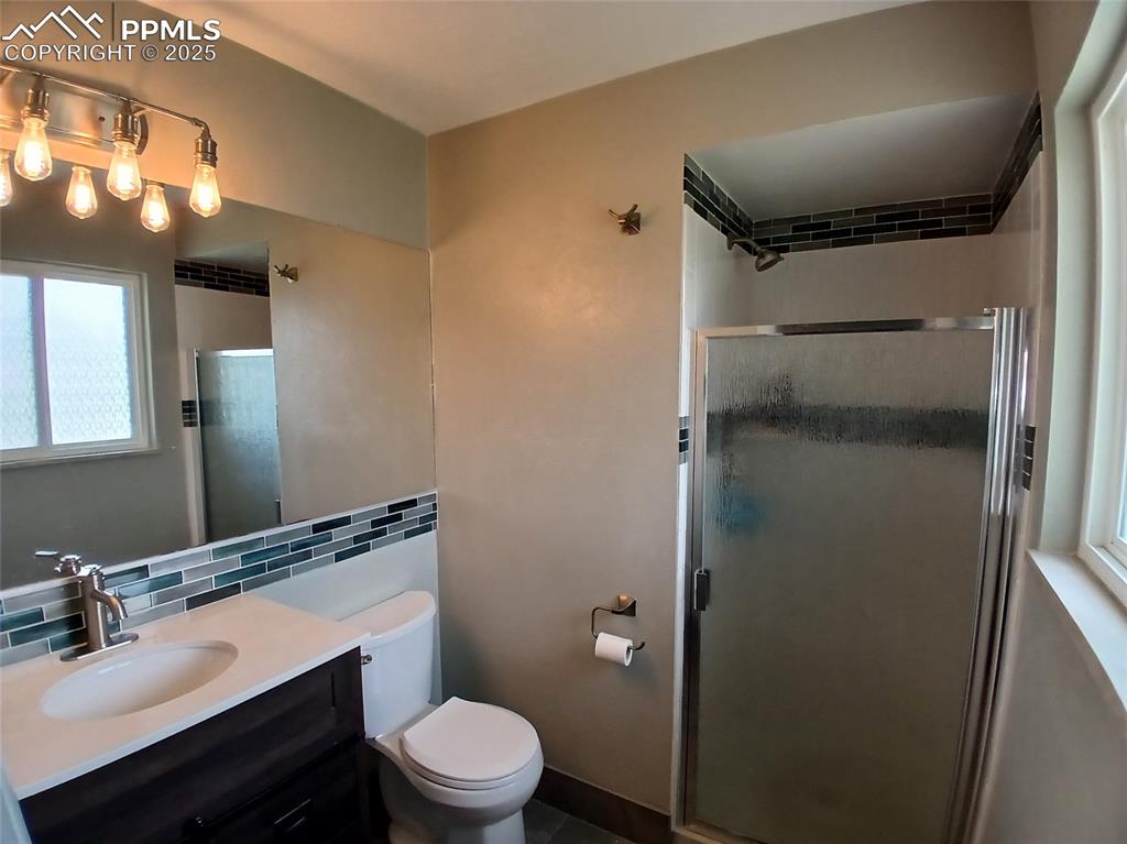 Bathroom featuring tile walls, backsplash, a shower with door, vanity, and toilet