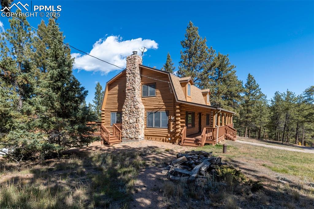 View of front of property featuring a gambrel roof, log exterior, a chimney, and a porch