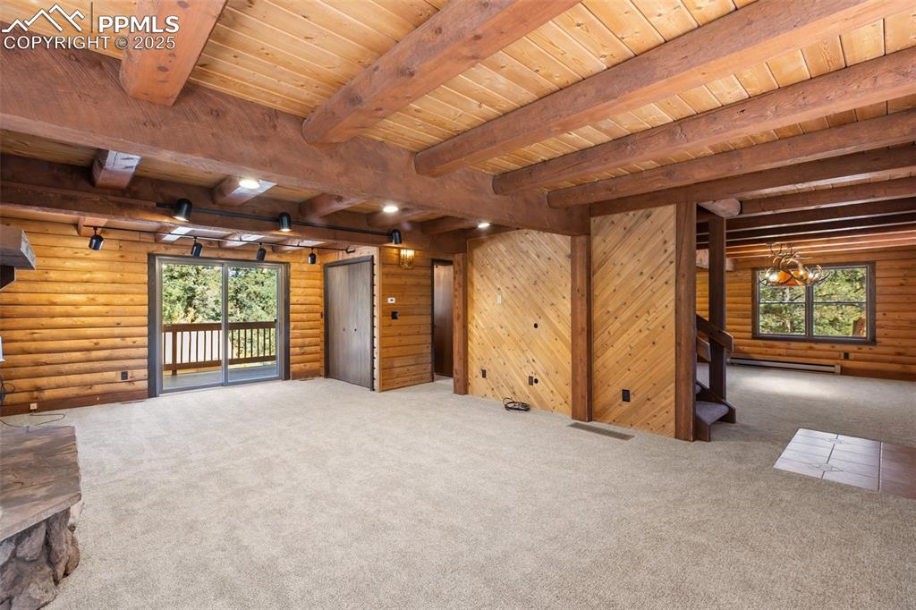 Living room view to side deck, and dining room. Living area featuring log walls, a wood-burning stone fireplace, new carpeting, and tongue & groove ceiling with exposed beams.