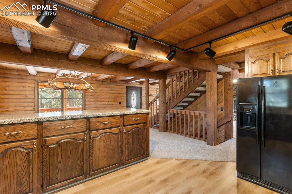 Kitchen with track lighting, black fridge, a wooden ceiling with exposed beams, light wood-style floors, and light stone counters