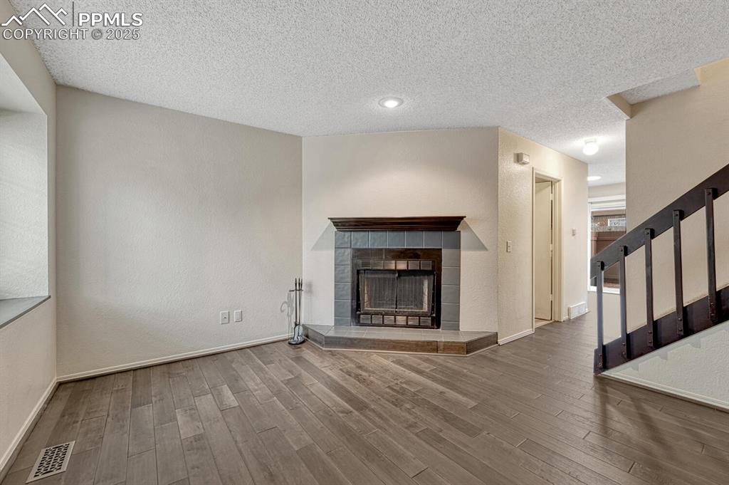 Unfurnished living room with a textured ceiling, wood finished floors, a tile fireplace, and stairway