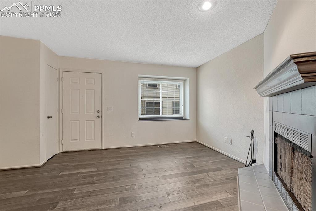 Unfurnished living room featuring wood finished floors, a textured ceiling, and a tile fireplace