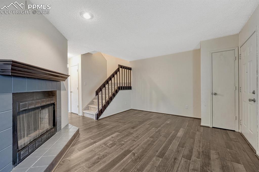 Unfurnished living room featuring wood finished floors, a textured ceiling, a fireplace, and stairs