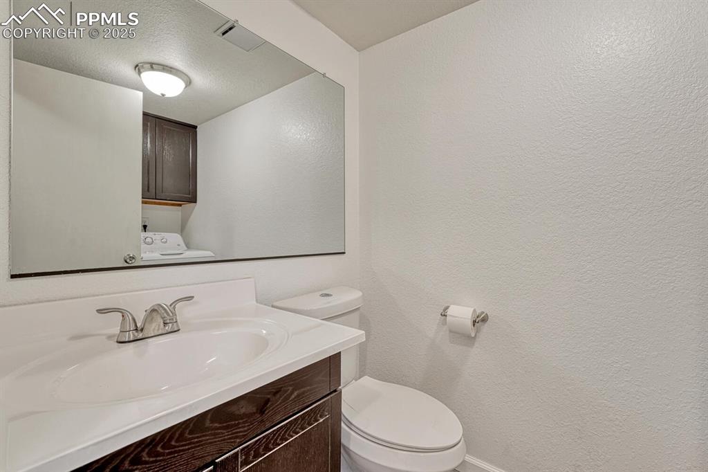 Half bath featuring vanity, a textured ceiling, a textured wall, and washer / clothes dryer