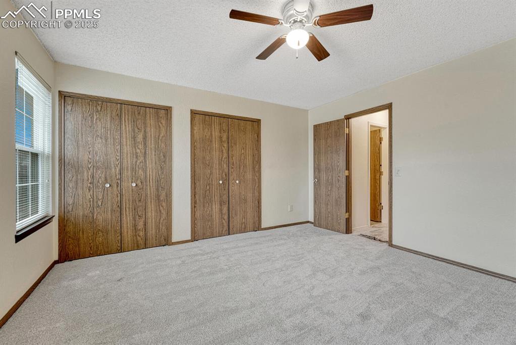 Unfurnished bedroom with multiple closets, a textured ceiling, carpet flooring, and ceiling fan