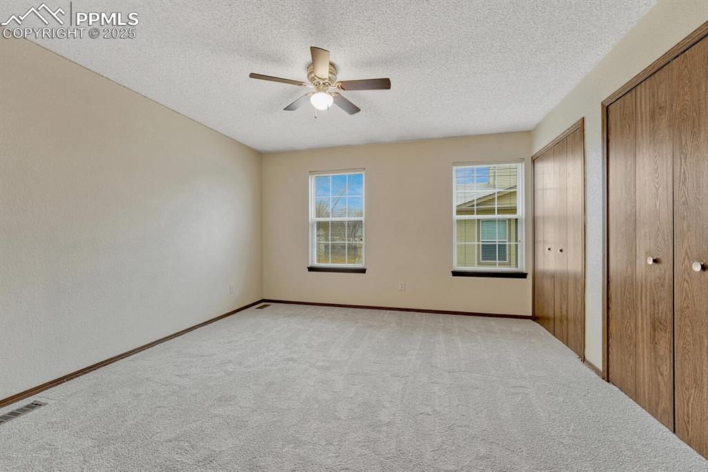 Unfurnished bedroom with multiple closets, carpet floors, a textured ceiling, and a ceiling fan