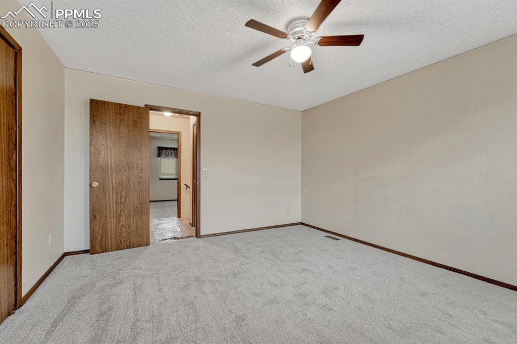 Empty room featuring a textured ceiling, a ceiling fan, and carpet