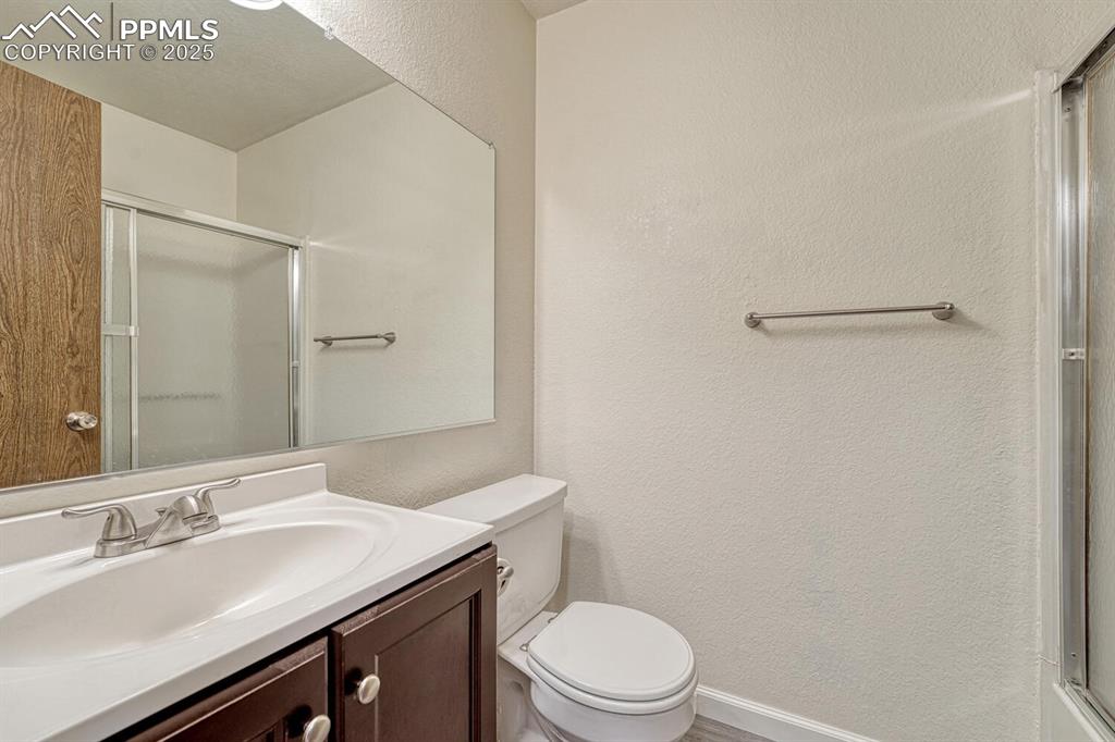 Full bath featuring a shower with shower door, a textured wall, and vanity