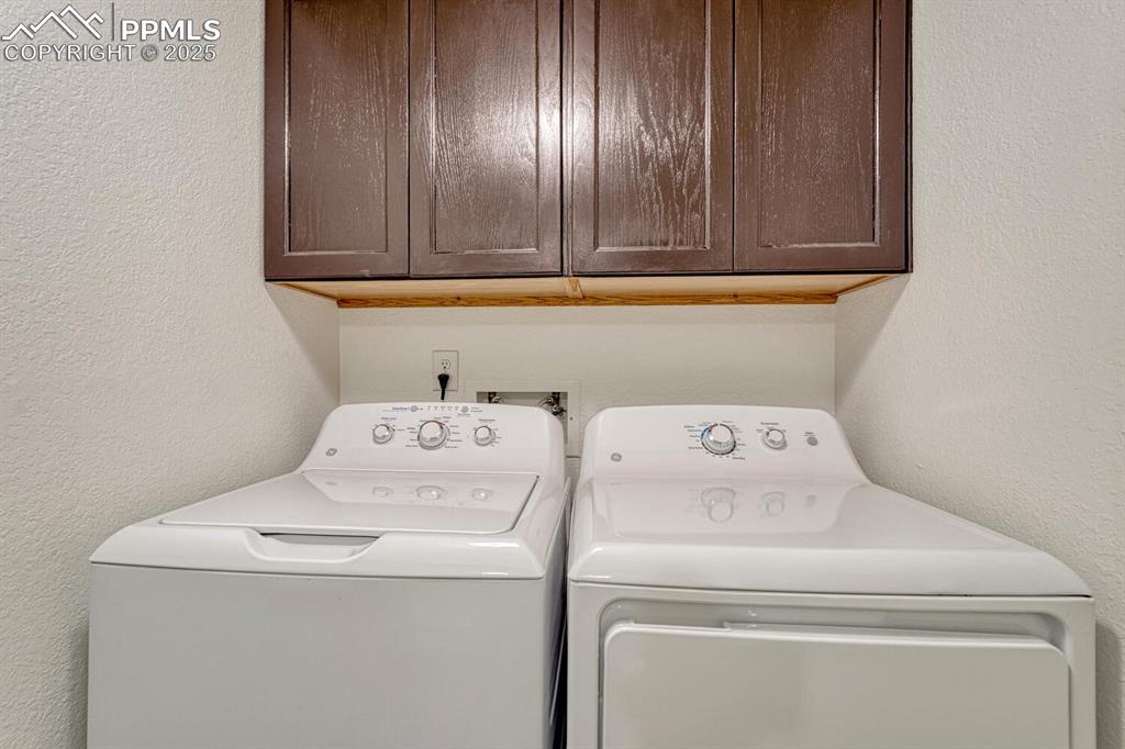 Washroom featuring a textured wall, cabinet space, and washer and clothes dryer