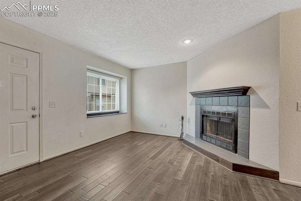 Unfurnished living room featuring a tiled fireplace, a textured ceiling, and wood finished floors