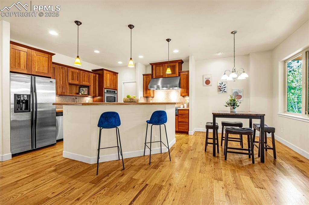 Kitchen with appliances with stainless steel finishes, ventilation hood, tasteful backsplash, a kitchen bar, and light wood-type flooring