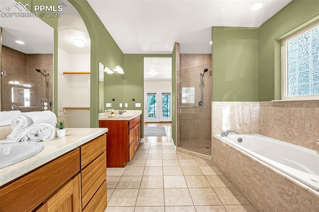 Full bath featuring a shower stall, two vanities, a garden tub, and tile patterned flooring