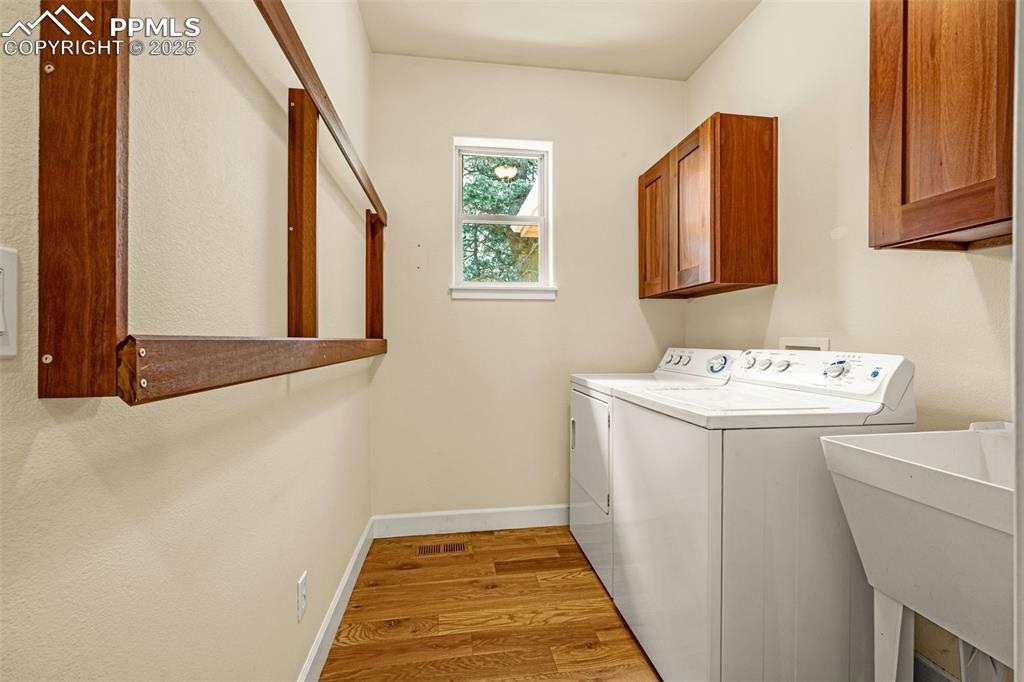 Washroom with washer and dryer, cabinet space, wood finished floors, and baseboards
