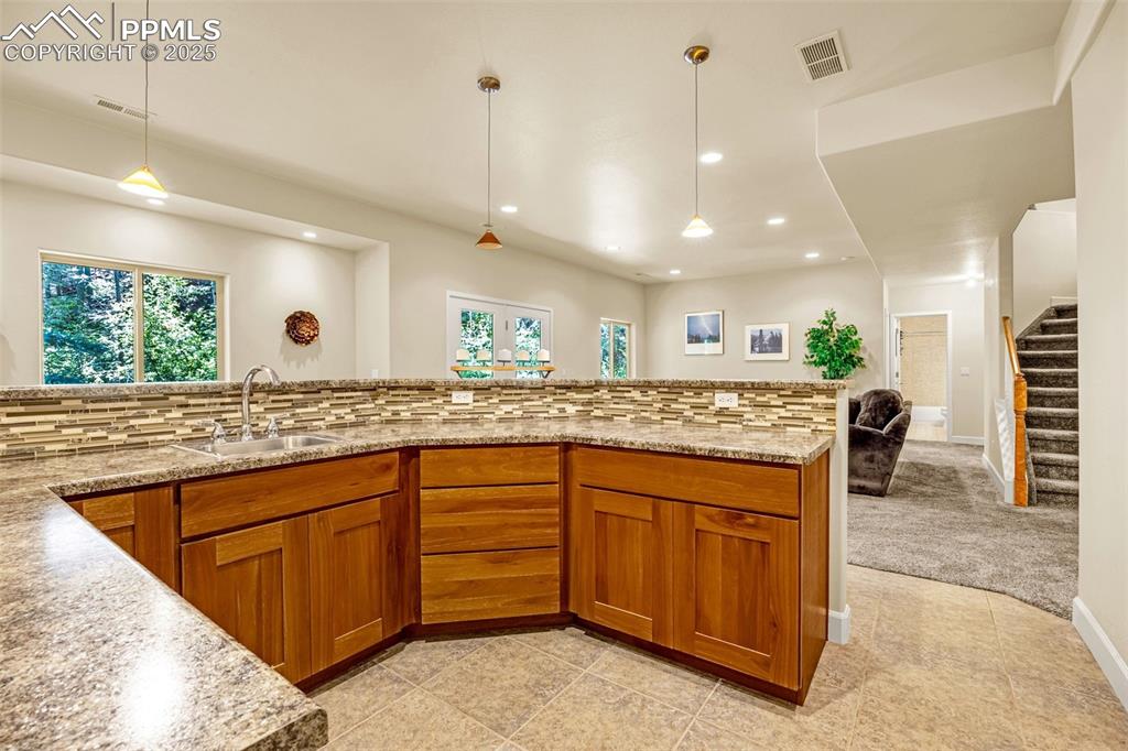 Kitchen with a sink, brown cabinetry, recessed lighting, plenty of natural light, and light stone countertops